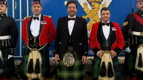 PA Media A row of men, including Jimmy Fallon, wearing kilts standing in front of a sign which reads 'His Majesty the King's Royal Guard'.