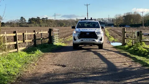A police truck is parked along a pathway leading towards a farm