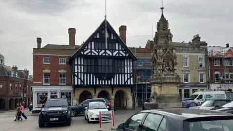 Henry Godfrey-Evans/BBC Tudor building and a fountain with parked cars surrounding