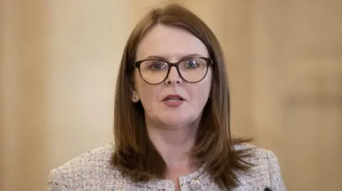 Liam McBurney / PA Wire Caoimhe Archibald wearing glasses and a cream tweed jacket.  She is looking to camera and is mid-speech