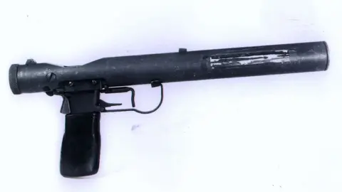 British Resistance Museum A World War Two pistol against a white background. It has a long tubular barrel and a short handle. 