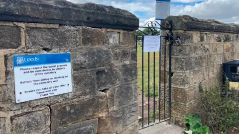 A stone wall with warning signs, divided by a small metal gate.