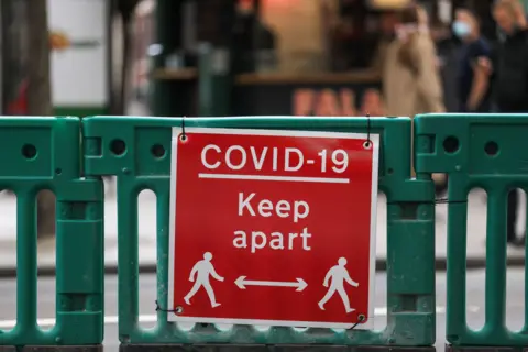A Covid-19 sign which is red with white writing. It says "Covid-19 Keep apart. It has figures of two people and an straight line with two arrows inbetween them. 