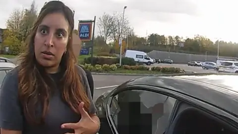 CCTV footage of a woman standing next to a black BMW in a supermarket car park