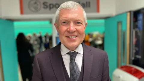 PA Media A man smiles while wearing a suit