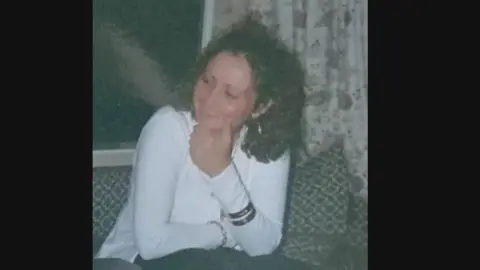 Cambridgeshire Police Woman with long dark hair, wearing white top, holding chin with left hand