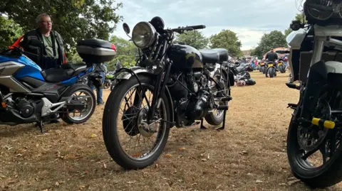 A photo taken from low down of three motorcycles parked in a line on a grass field. 
