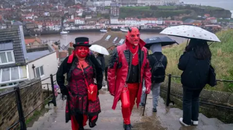 Danny Lawson/PA A man and a woman in red face paint and gothic clothing walk up Whitby steps