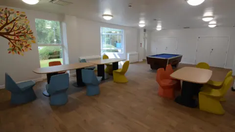 Leicestershire Partnership NHS Trust A room with a wooden floor, white walls and tables with colourful tables around them.