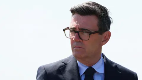 PA Andy Burnham wearing a dark suit and glasses.
