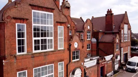 The Seagull A drone image of the Seagull Theatre. It is a large red brick building with a white van parked outside. 