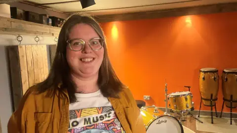 Photograph of Laura Howkins from Voltalab Studios in Rochdale. She is pictured in front of a drum kit.