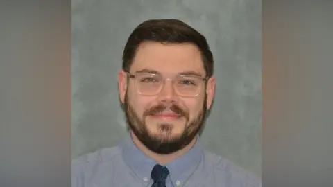 Suffolk Police A head and shoulders image of a man wearing a blue shirt and tie and glasses. He is looking into the camera.