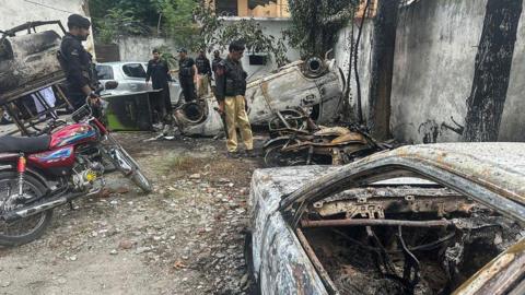 Policemen inspect the burned vehicles at a police station in the Madian area of Swat Valley on June 21, 2024, a day after an angry mob stormed the police station where the man had been detained after being accused of burning the Koran. 