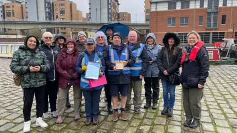 Mark Ansell / BBC Four walk volunteers with blue vests high visibility vests on and several members of the public who've attended the walks at Victoria Quays in Sheffield.