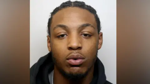Dino Donaldson, a young man with a goatee beard, stares into a camera for a police custody photo.