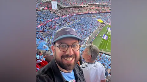 James Roach A man in a Coventry City top in the upper tier at Wembley Stadium.