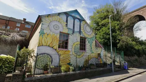 A detached building with pink window frames and large sunflowers painted on it.