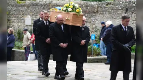PA Media Men in black suits carrying a wooden coffin on their shoulders.