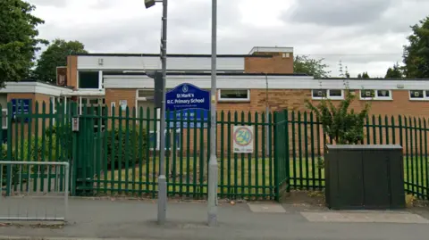 The exterior of a primary school with green metal gates and a sign reading: 'St Mark's RC Primary School'