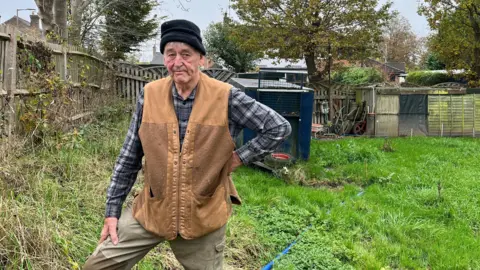 Tony Fisher/BBC The homeowner in a field with a pump behind him which drains the excess water off into the road.