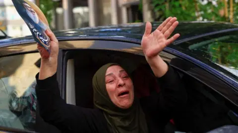 Reuters A woman reacts while holding a poster with an image of late Hezbollah leader Sayyed Hassan Nasrallah from inside a car, at the entrance of Beirut's southern suburbs, after a ceasefire between Israel and Iran-backed group Hezbollah took effect at 0200 GMT on Wednesday after U.S. President Joe Biden said both sides accepted an agreement brokered by the United States and France, in Lebanon, November 27, 2024.