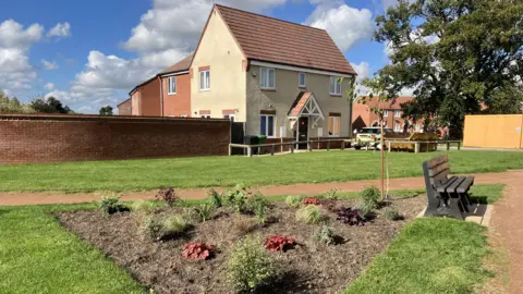 Memorial garden with a flower bed, new plants and a bench, near houses on the estate