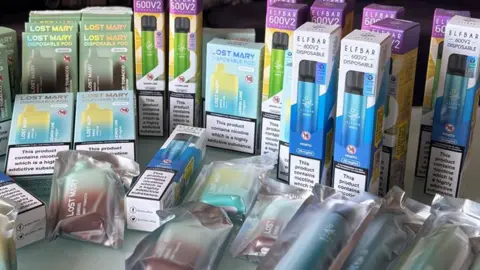 Cara Hallinan Close up of Cara's disposable vape stash. There are various brands like Elf Bar and Lost Mary. There are probably about 20 vapes in shot.