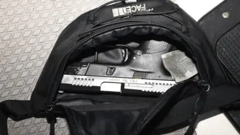 National Crime Agency A black North Face bum bag sits on a metal table. It is open and a black handgun is stored inside.