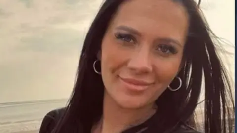 Police handout Headshot of a smiling Kiena Dawes, she has long brown hair and big hoop earrings and is standing on a beach