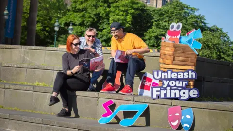 Three people reading Fringe programme in Edinburgh