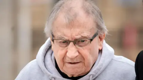 Kenneth Lingard arriving at Liverpool Crown Court in April 2025. He has grey receding hair and a moustache and is wearing glasses and a grey hoodie. 