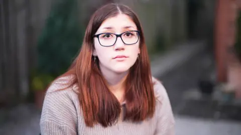 BBC A close-up portrait of Laura Kenny, facing the camera directly. She has long brown hair that falls past her shoulders and she is wearing dark-framed glasses. Her expression is calm and neutral.
