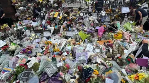 Hundreds of flowers and tributes to Ozzy Osbourne lie on the bench and floor on Black Sabbath Bridge.