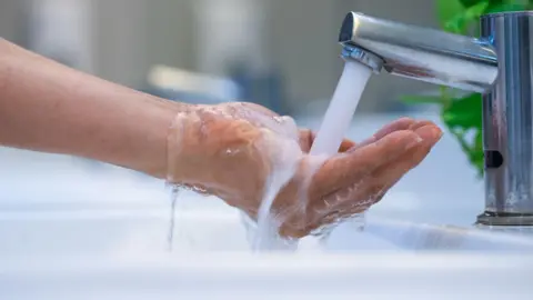 Getty Images A close up of hands cupped under a silver tap as water streams into them, spilling over into the sink below