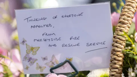 PA Media A card attached to flowers with butterflies on that reads thinking of everyone affected, from Merseyside Fire and Rescue Service.