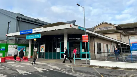 The main entrance to the Royal Cornwall Hospital, with a few people walking outside and a large sign saying 'Trelawny Wing'