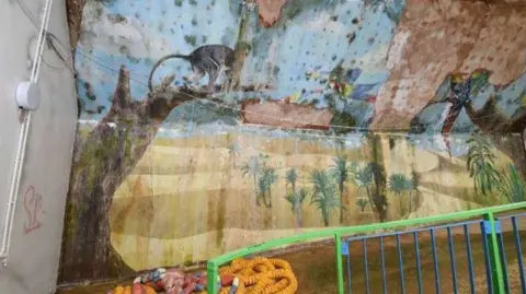 Historic Environment Consultancy A painting on a wall shows a monkey hanging on a tree with some birds flying nearby. The painting has been water damaged and is disfigured by mould.