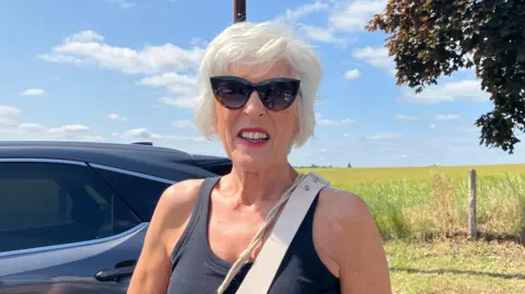 Susan Duffin wearing sunglasses smiling with her car and a field in the background
