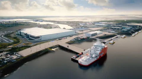 ABP An aerial view of BAE systems in Barrow, Cumbria. In the forefront of the photo a large ship is moored on a dock with several smaller ships behind. On land there is a vast white building with many other building behind and a river course leads to Cavendish dock 