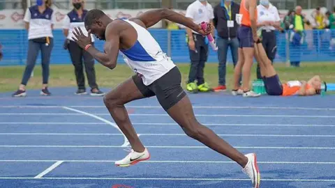 Frederick Afrifa Frederick Afrifa is running on an athletic track at an event. Others athletes are around watching. Some officials are also watching and wearing face masks.