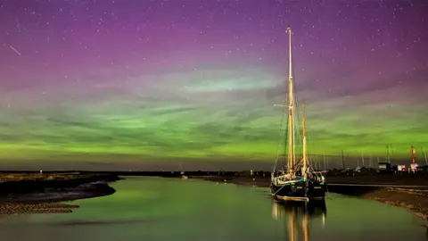 Boat in Blakeney harbour illuminated by green and purple Northern Lights in the sky