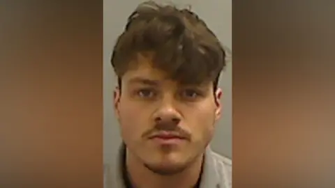 Mugshot of Walker. He has a moustache and faint goatee and thick brown hair, short at the sides and long over his forehead.