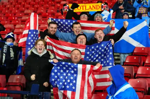 PA Media Scotland fans hold USA and Scotland flags in the stand and celebrate