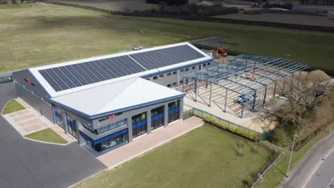 Delta Fire An aerial view of Delta Fire. The main building is L shaped. It has a solar panelled roof. The building has a steel frame outside it, suggesting an extension is under way