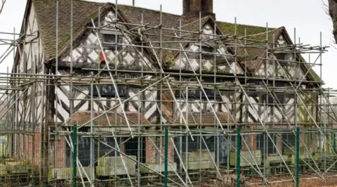A black and white timbered building surround in scaffolding.