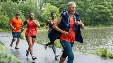 Four people running in the rain next to a body of water. They are wearing bright coloured running clothes.