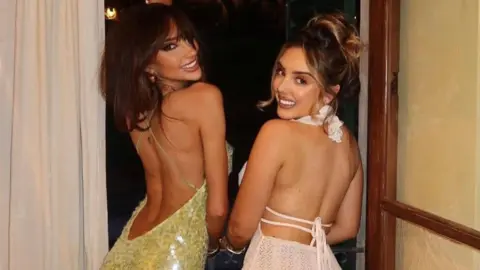 Caramella Mollie-May Rossi is wearing a cream backless, halterneck dress next to Ellie Edgar, who is wearing a yellow dress embellished with sequins. 