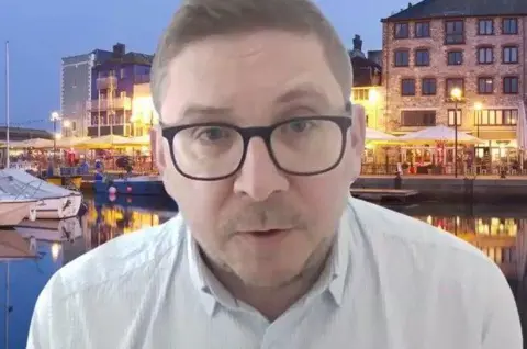 Rob Witton is wearing a white shirt and black-rimmed glasses