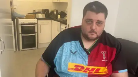 Nathan Rollinson - a man with short brown hair and brown stubble. He is wearing a red, blue and black Harlequins top looking into the camera.